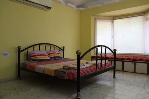 Free Inviting bedroom interior in Ahmedabad, featuring a metal bed, yellow walls, and cozy window seating. Stock Photo