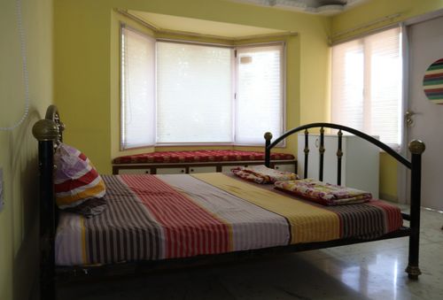 Free Bright bedroom interior with a striped bedspread, bay windows, and colorful decor, perfect for a cozy ambiance. Stock Photo