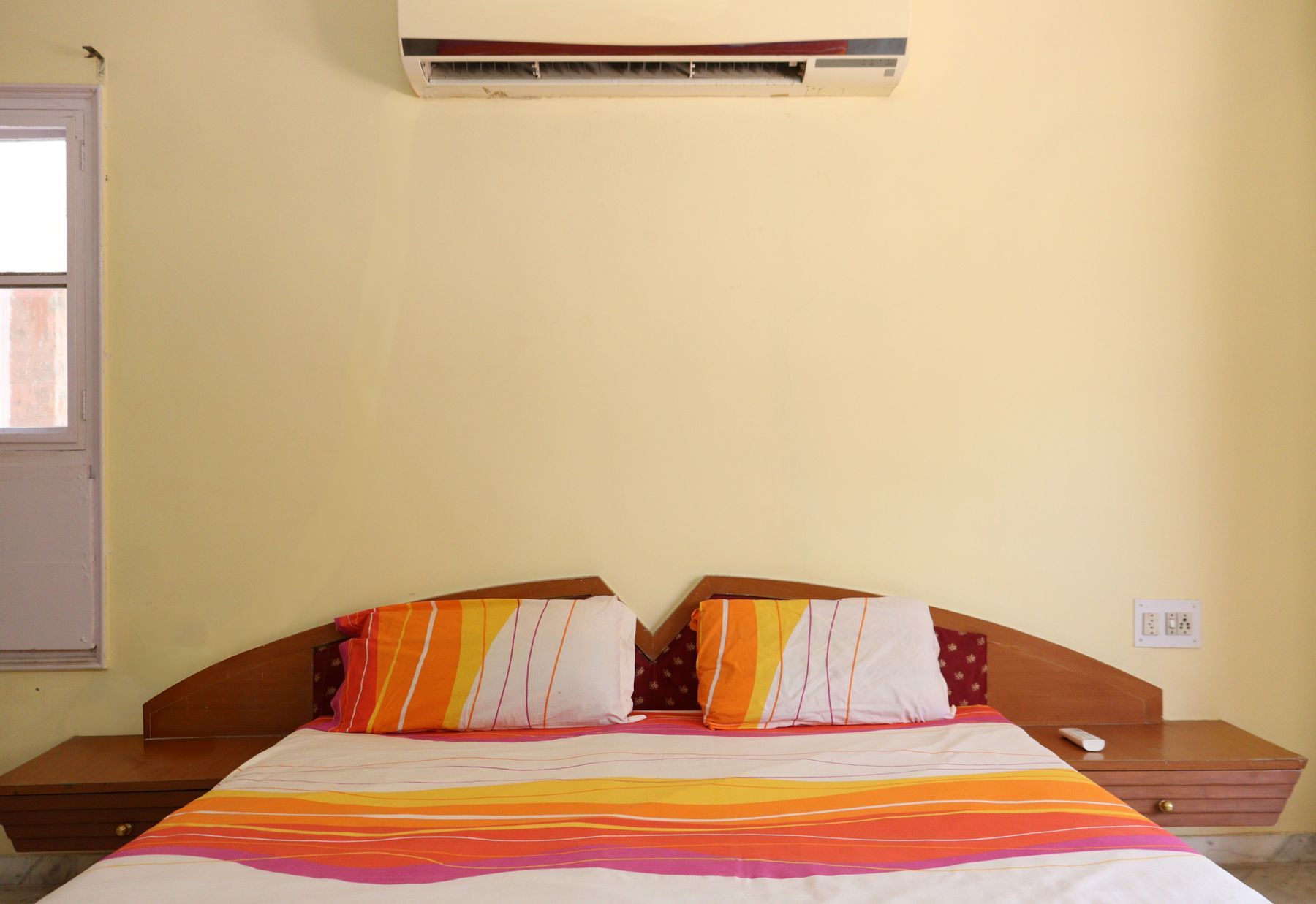 Shared bedroom with pale yellow walls, black metal beds, striped bedding, window and wall-mounted air conditioner