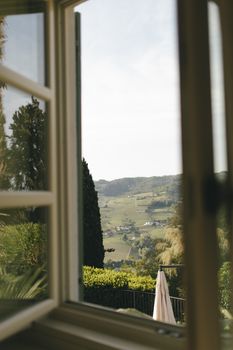 Beautiful countryside landscape viewed through an open window, capturing lush greenery and hills.