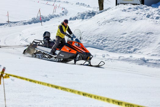 A man on an orange snowmobile traverses a snowy terrain in Hokkaido, Japan.