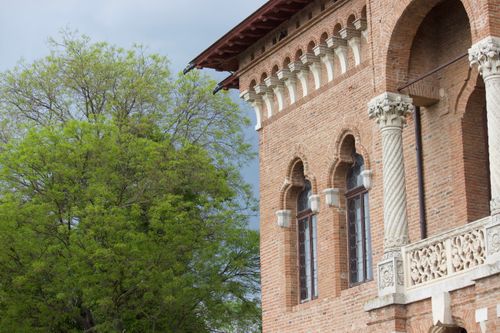 Free Image of a brick building with arched windows and ornate columns beside a green tree. Stock Photo