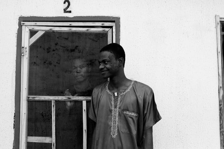 Cheerful Ethnic Man Standing Near Friend Looking Through Window