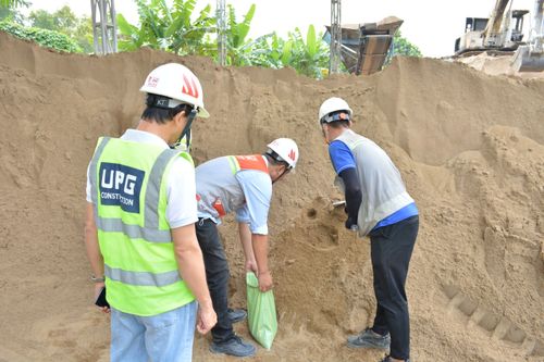 Free A group of construction workers wearing safety gear inspect a large sand pile on site. Stock Photo