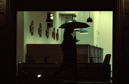 Free Silhouette of a person with an umbrella walking past a lit interior at night in Kutaisi, Georgia. Stock Photo