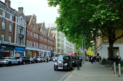 Free Lively urban scene with classic buildings, taxis, and bustling pedestrian activity. Stock Photo