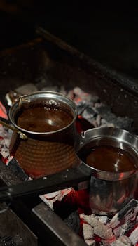 Two pots of coffee brewing on a glowing charcoal bed, showcasing traditional methods.