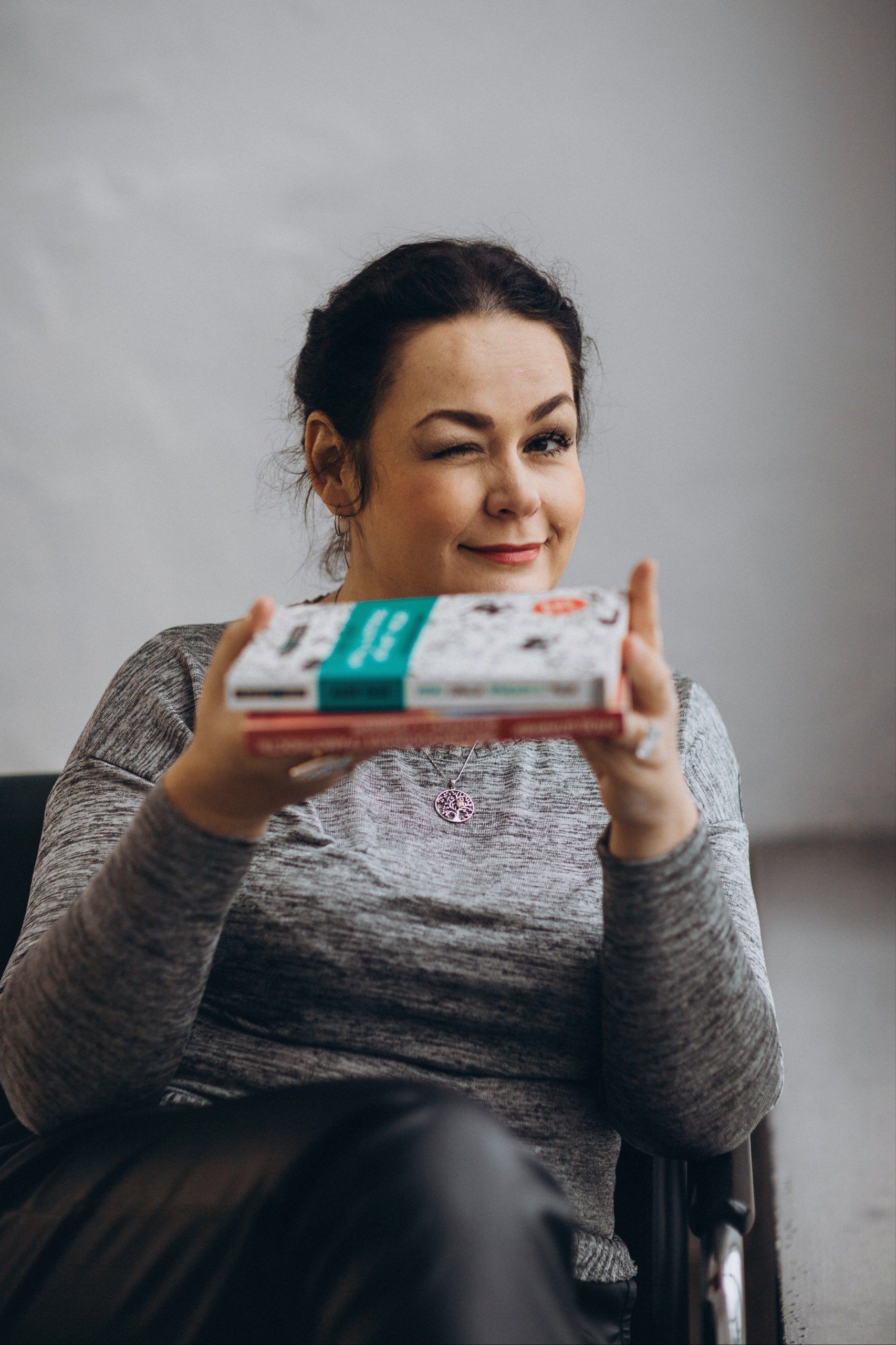A cheerful woman winks while holding pizza boxes, suggesting a relaxed indoor setting.