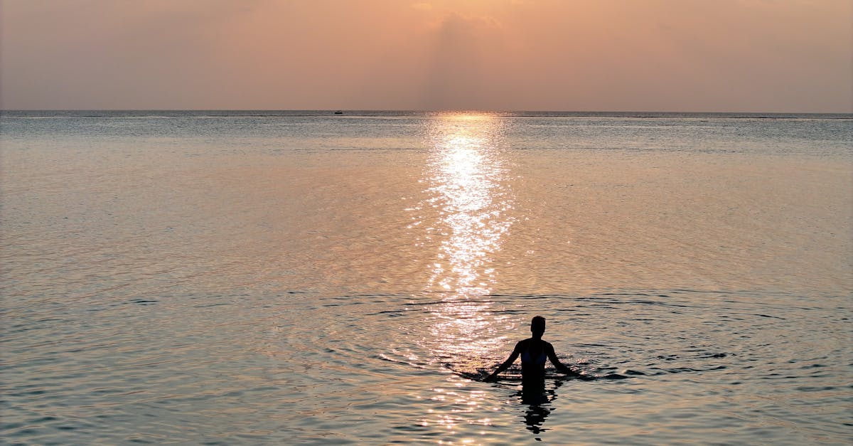 A lone swimmer enjoys a tranquil sunset at Thoddoo Beach, Maldives, surrounded by calm ocean waters.