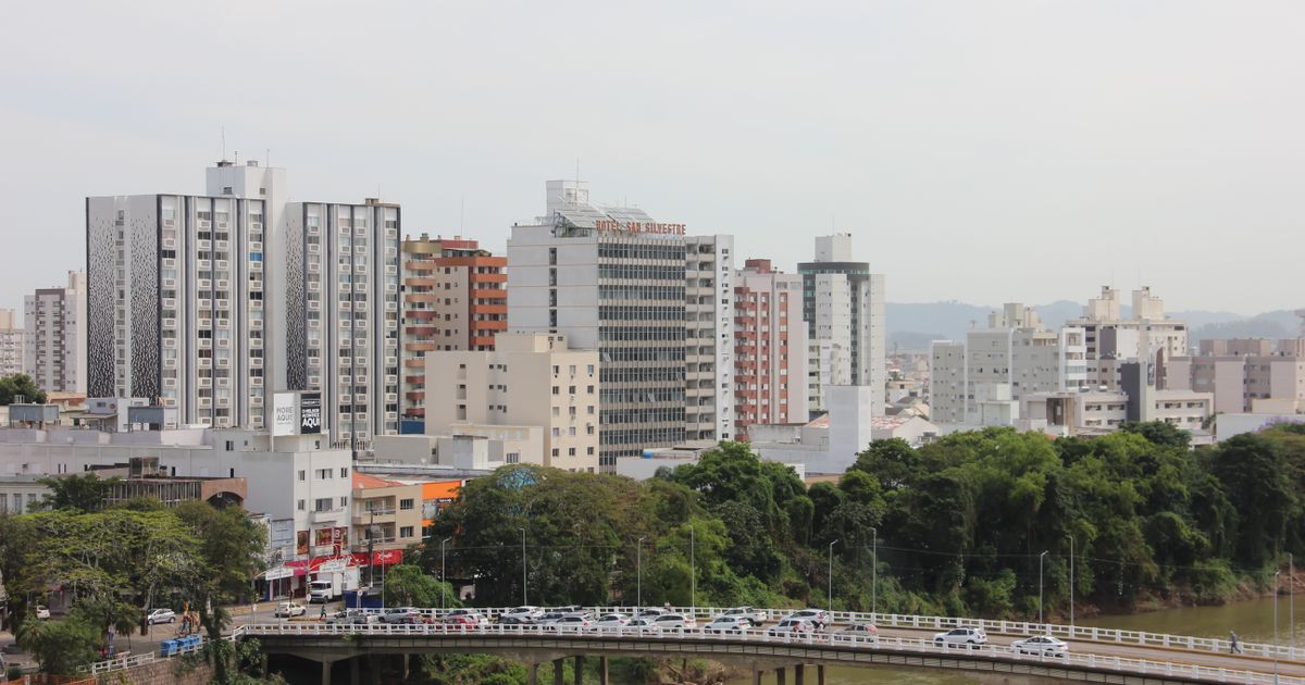 Uma paisagem urbana movimentada com edifícios altos e uma ponte cruzando um rio em um dia claro.