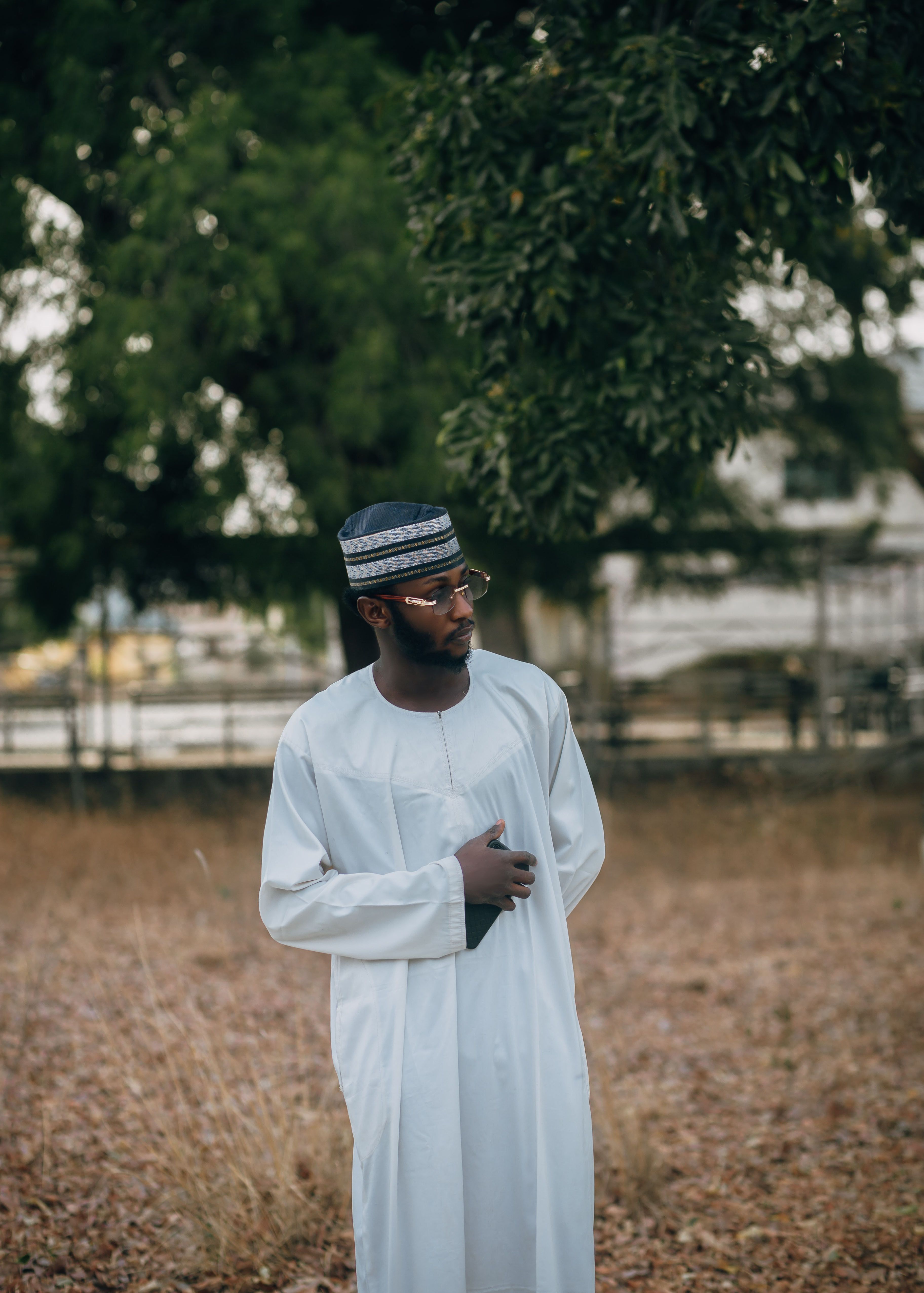 A man in traditional attire stands outdoors in a serene environment, showcasing cultural fashion.