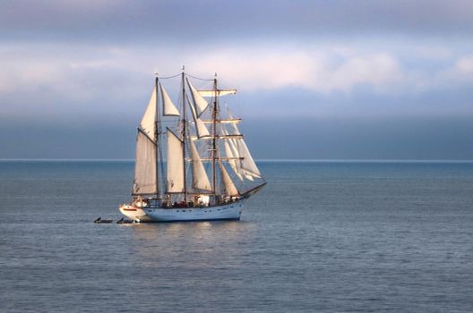 A stunning tall ship sails the calm waters of Granville, Normandie, France, under a serene sky.