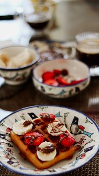 Close-up of a waffle topped with strawberries, bananas, and chocolate in a patterned dish.