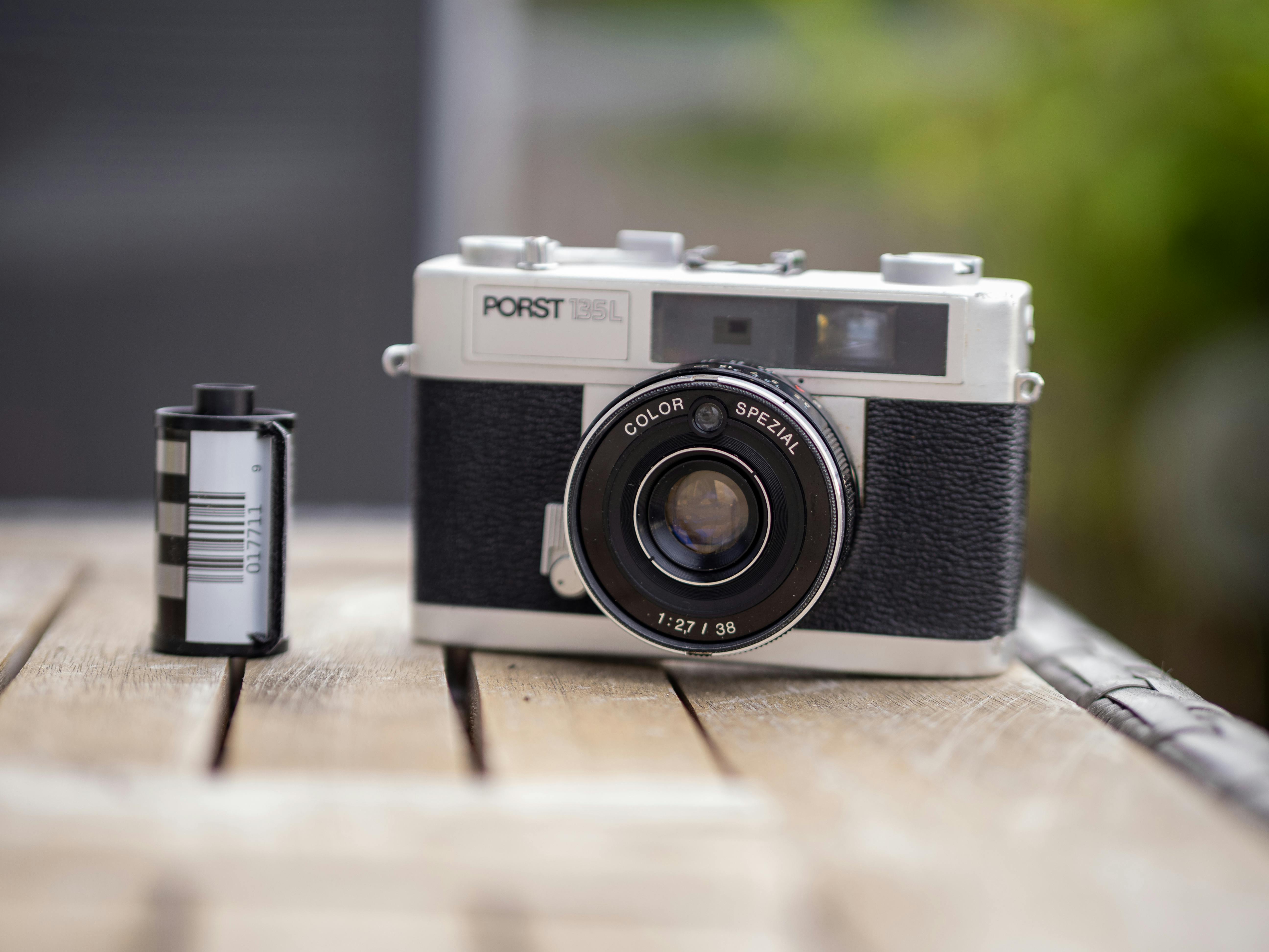 Close-up of a vintage film camera next to a roll on a rustic wooden table outdoors.