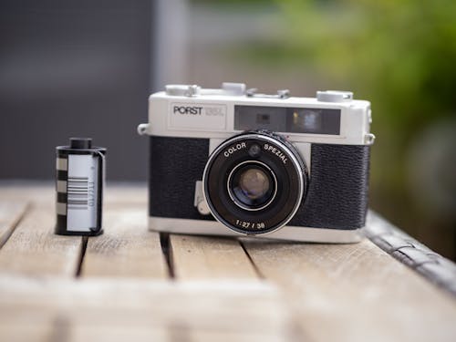 Free Close-up of a vintage film camera next to a roll on a rustic wooden table outdoors. Stock Photo