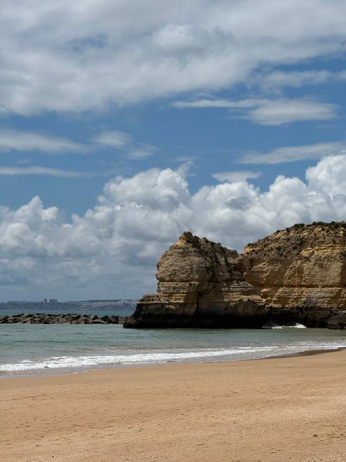 Free Tranquil beach scene with rocky cliffs and gentle waves under a cloudy blue sky. Stock Photo