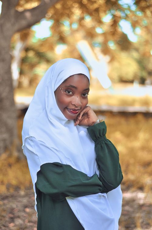 Free Portrait of a smiling woman in hijab standing outdoors in a park-like setting during fall. Stock Photo