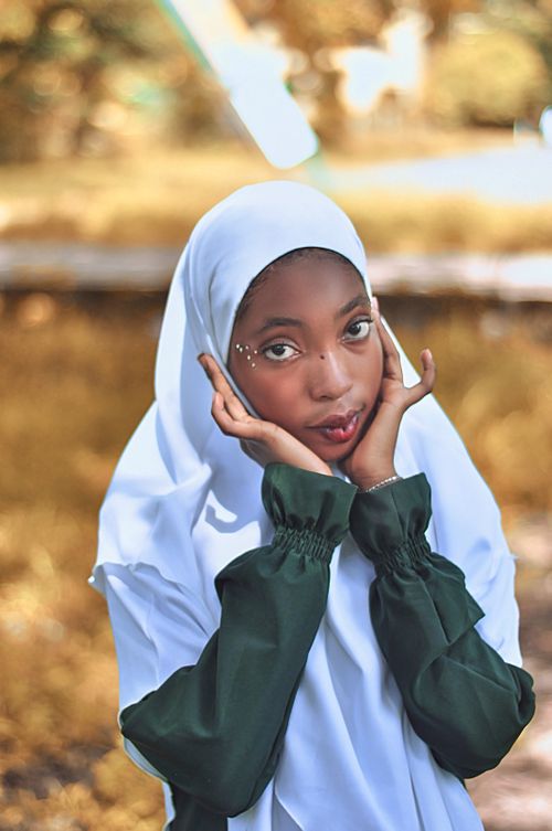 Free Portrait of a young woman in a green and white hijab posing thoughtfully in a natural outdoor setting. Stock Photo