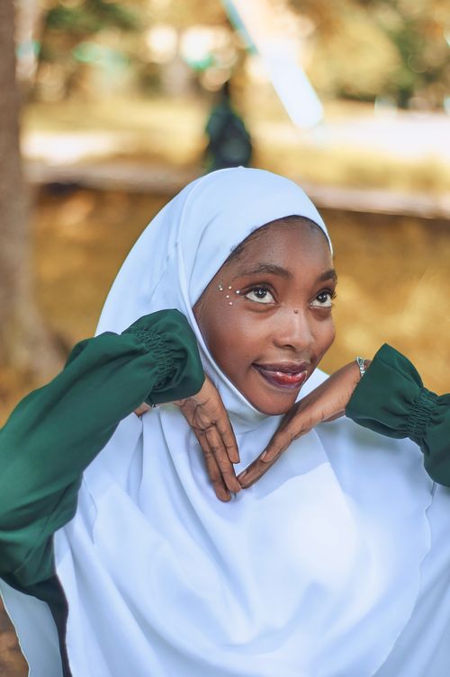 Free Joyful young woman wearing a hijab and looking upward with a smile in a sunny outdoor setting. Stock Photo