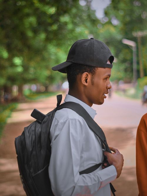 Free Side profile of a young man wearing a cap and backpack walking in a green urban park. Stock Photo