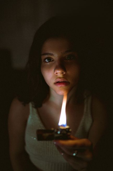 A woman holding a lighter, casting a dramatic glow on her face in a dimly lit room.
