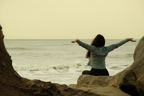 Free A person enjoys a tranquil sunset at a rocky beach, embracing the ocean view. Stock Photo