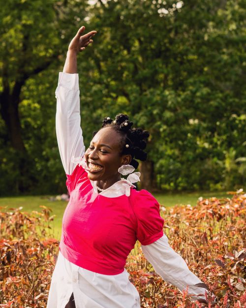 Free Smiling woman in vibrant clothing enjoying a dance amidst green and autumn foliage. Stock Photo
