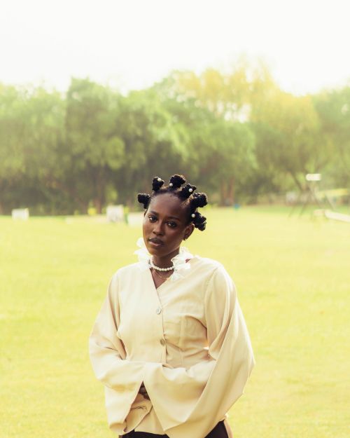 Free A young woman in a park wears a cream blouse and styled hair, exuding confidence and modern fashion. Stock Photo