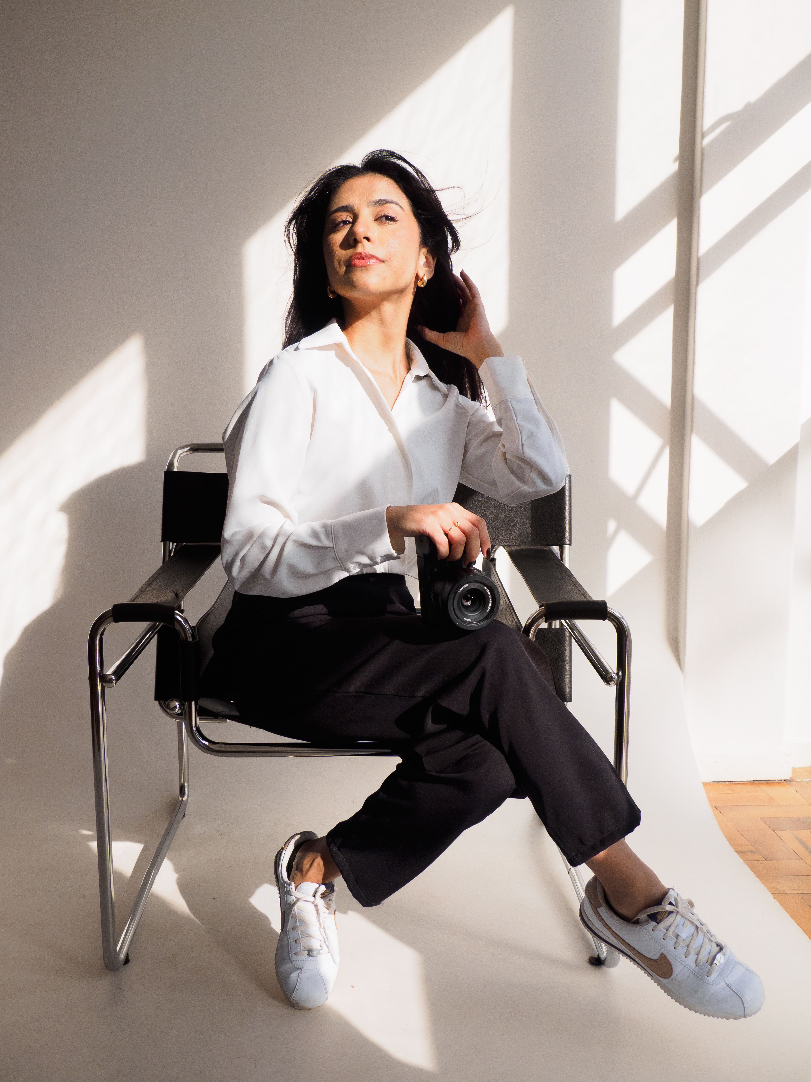 Portrait of a confident photographer seated stylishly, holding camera in bright natural light.