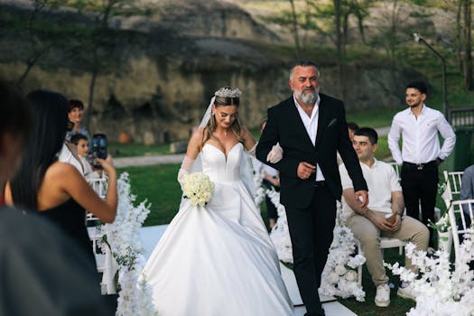 A beautiful bride walks down the aisle with her father during an outdoor wedding ceremony.
