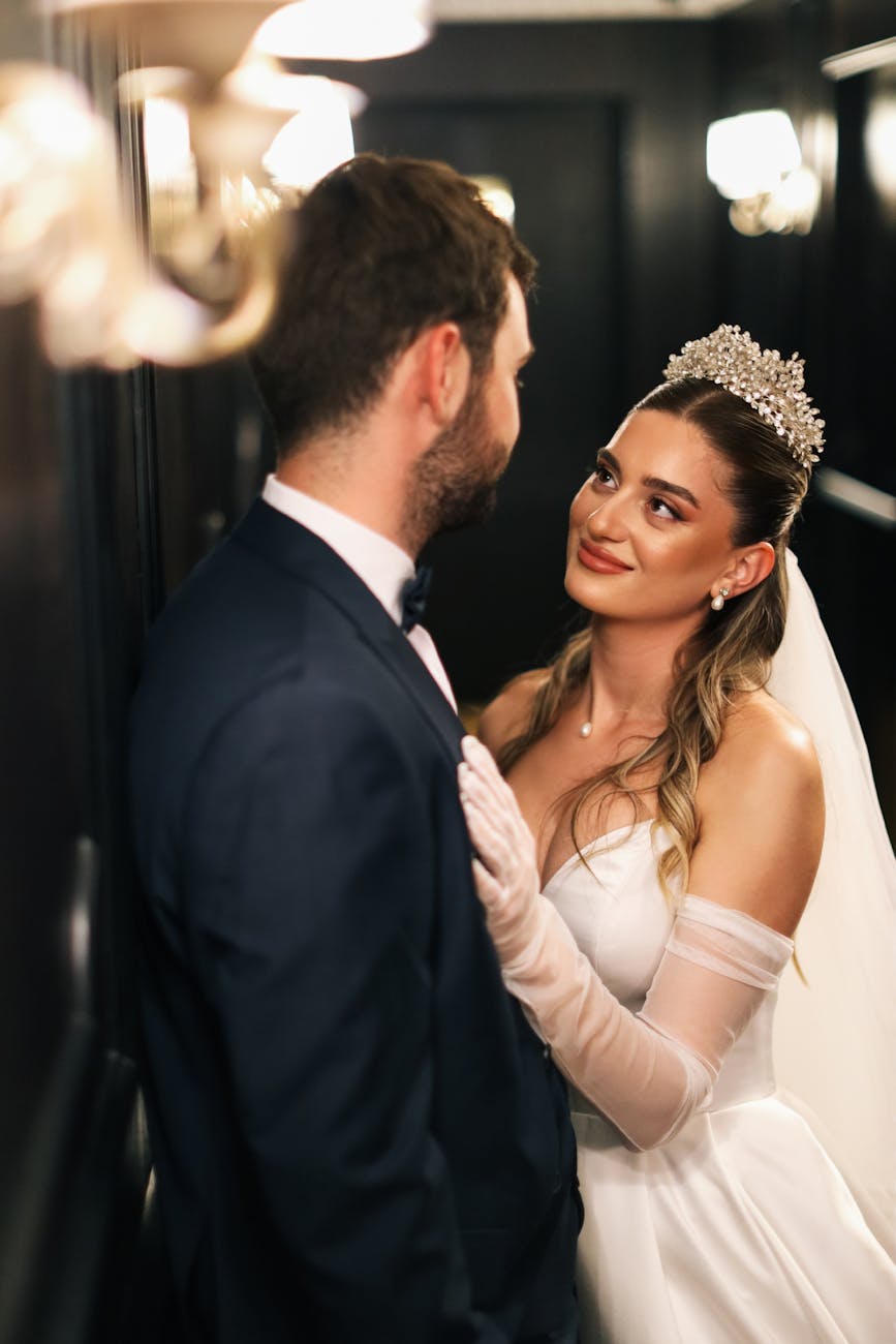 Romantic indoor wedding photo of bride and groom gazing at each other, dressed elegantly.