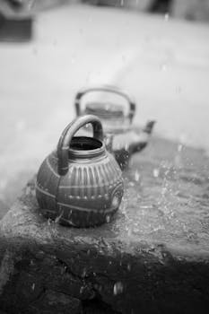Monochrome image of kettles on stone under falling rain, artistic mood.