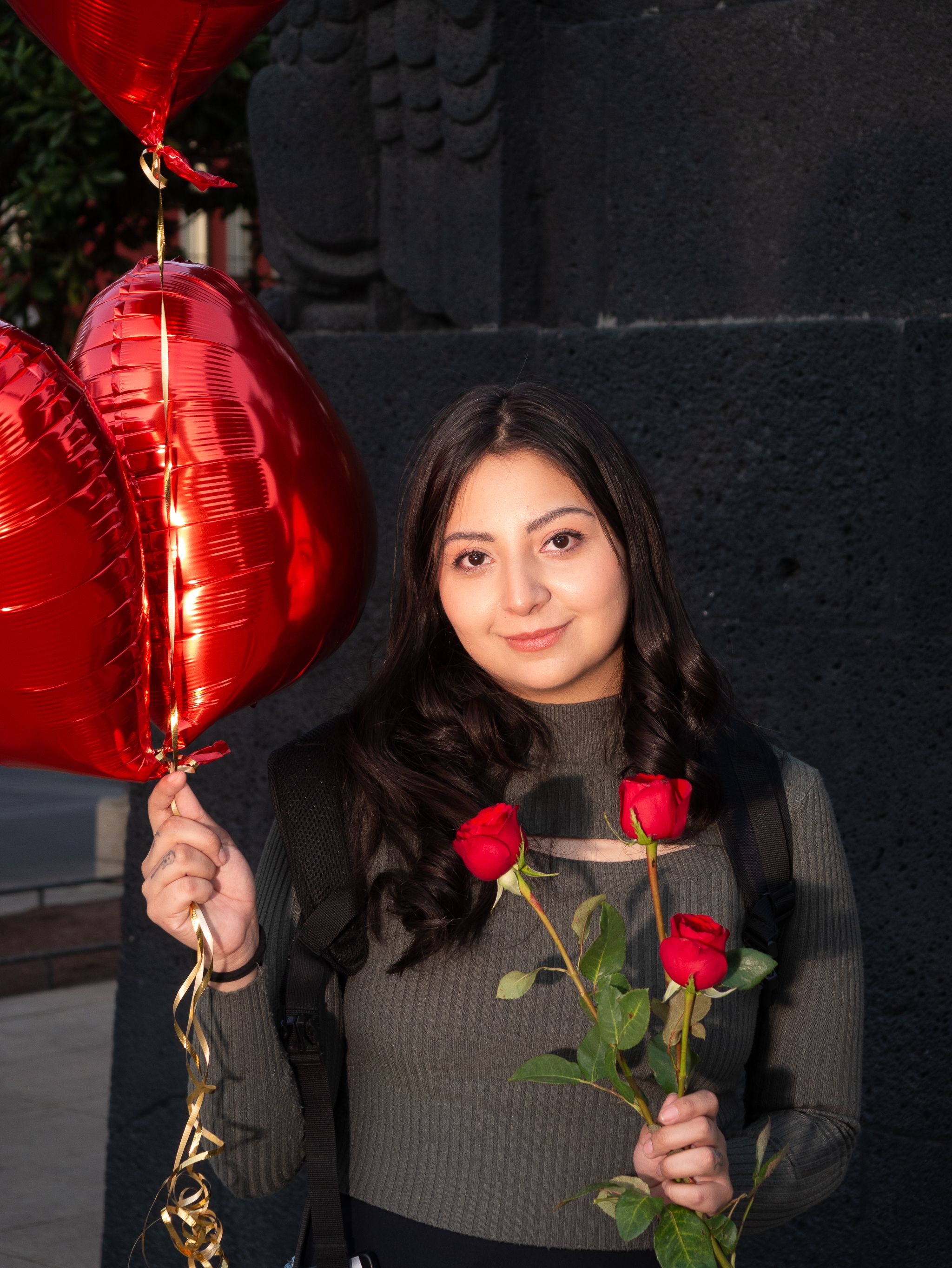 A young woman holding red balloons and roses against an urban backdrop in Mexico City.