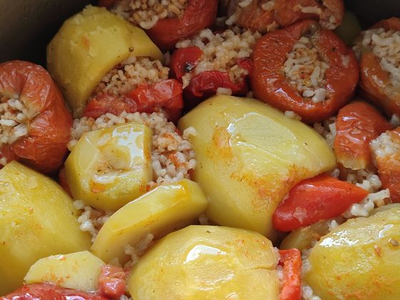 Baked tomatoes and peppers stuffed with herbed rice nestled between glossy potato wedges