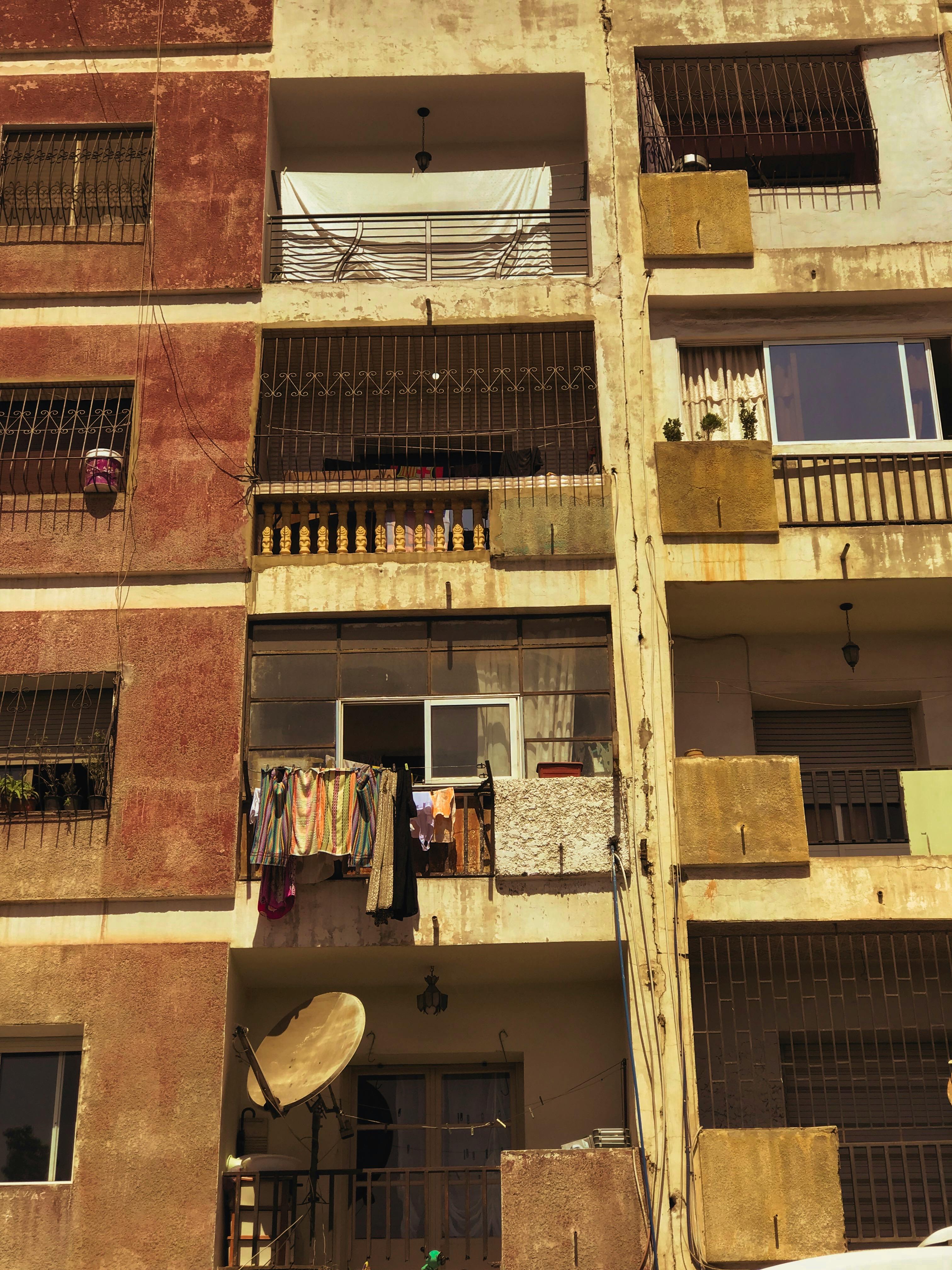 Facade of an urban apartment building with hanging laundry and satellite dish, daytime.