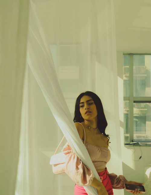 Free Elegant woman by a window in soft, warm light, wearing pastel and pink tones indoors. Stock Photo
