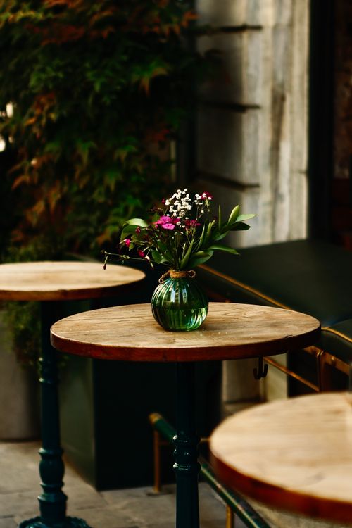 Free Rustic cafe table adorned with a small bouquet in a green vase outdoors. Stock Photo