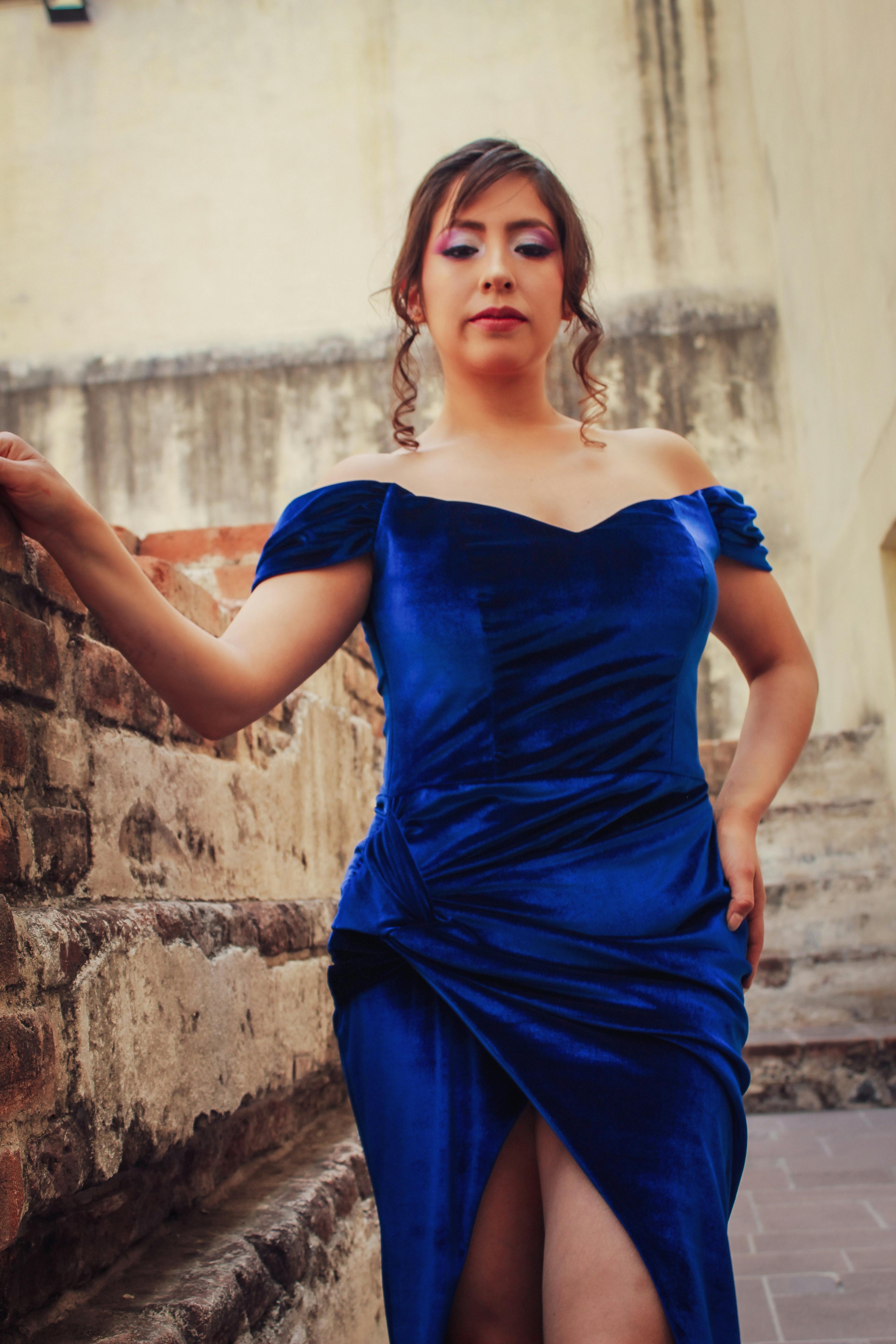 Gratis Una donna in un elegante abito da sera blu posa con sicurezza in un ambiente interno illuminato da luce naturale. Foto a disposizione