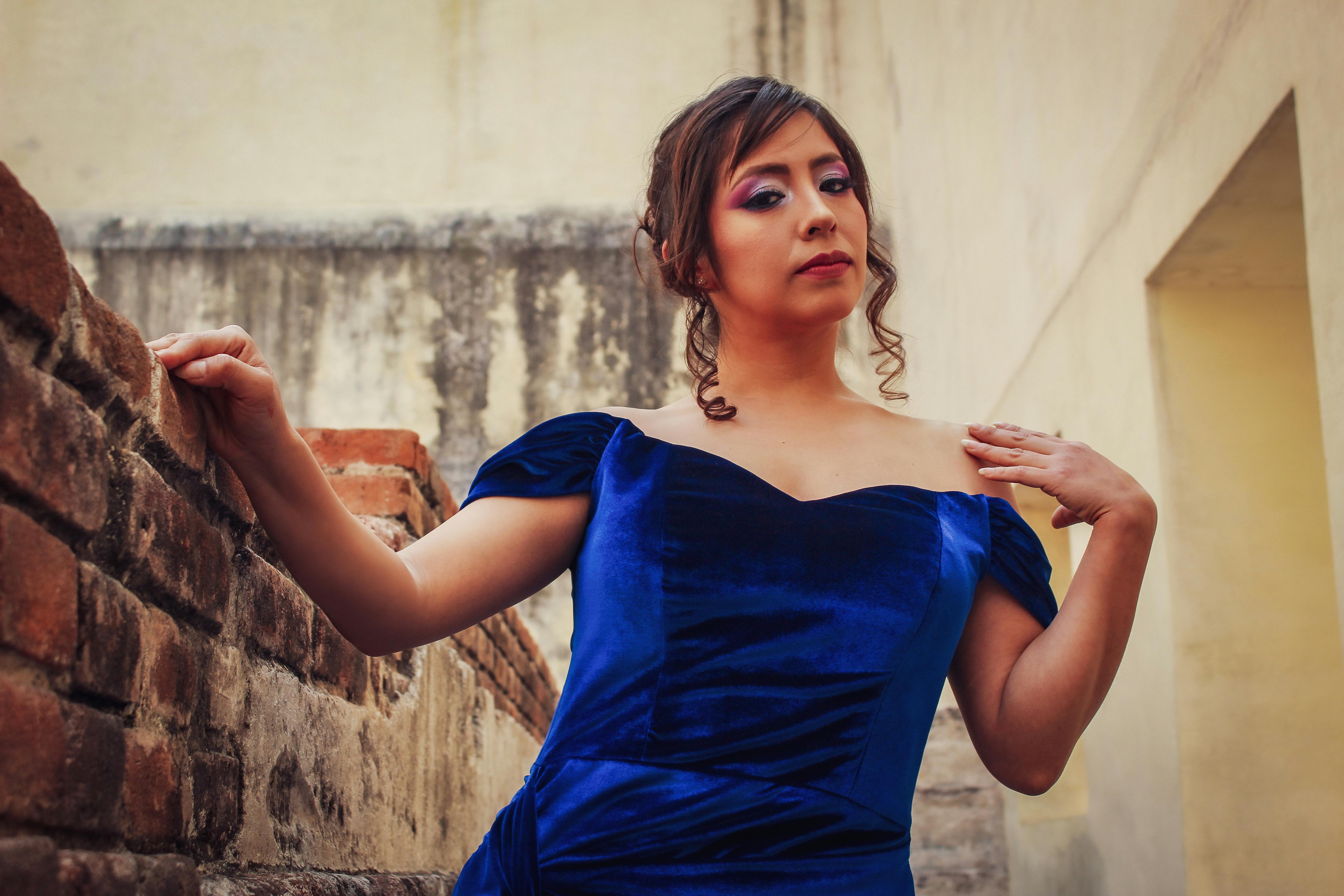 bezplatná Stylová žena v modrých sametových šatech pózuje venku u cihlové zdi. Základová fotografie