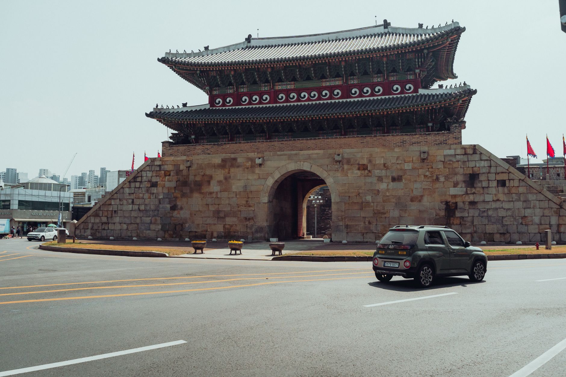 A historic Korean gate in Seoul with a modern car passing by, blending tradition with modernity.