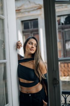 Fashionable young woman posing indoors with natural window light, showcasing modern style.