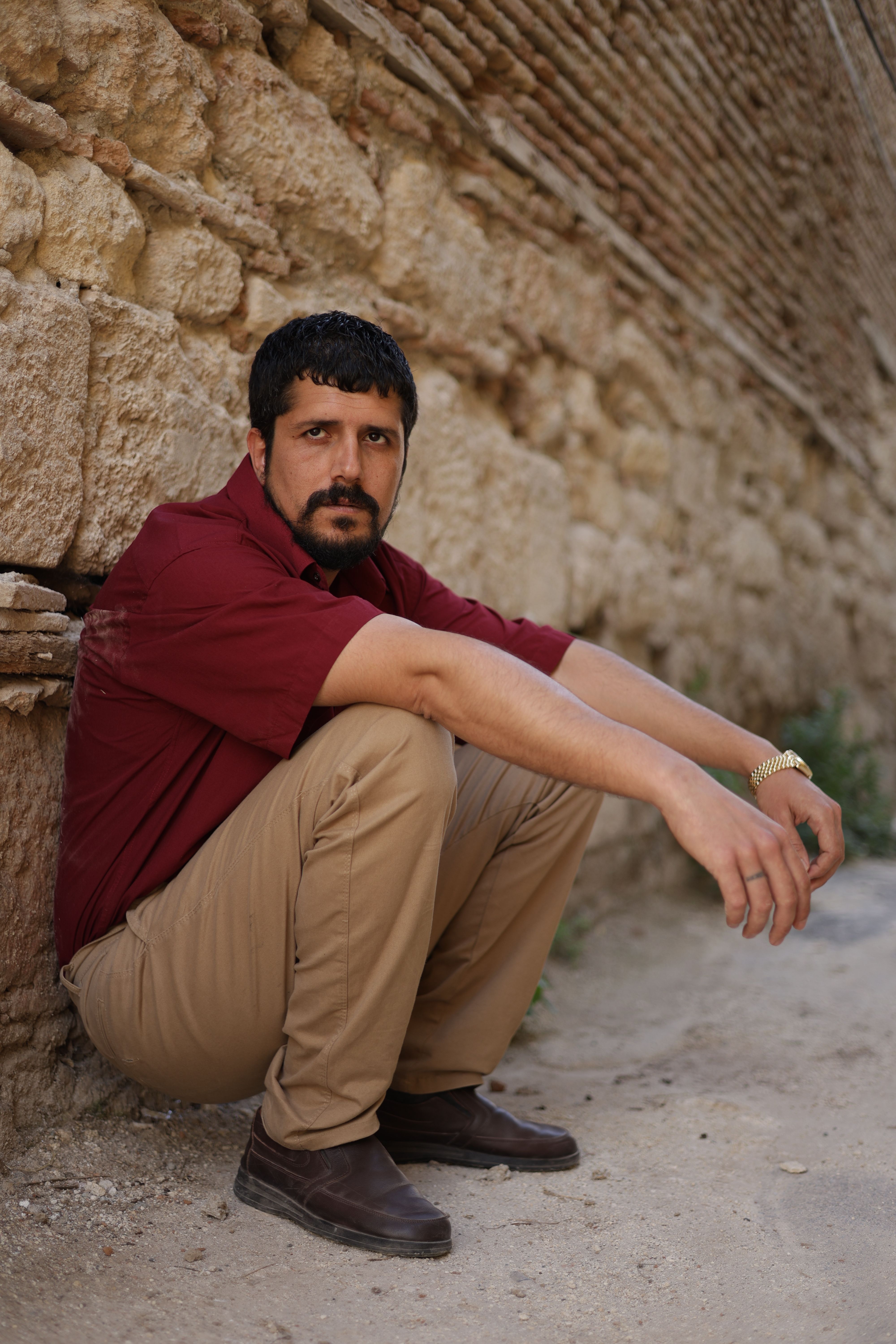 Man in casual attire poses by an ancient stone wall in Türkiye, showcasing historic architecture.