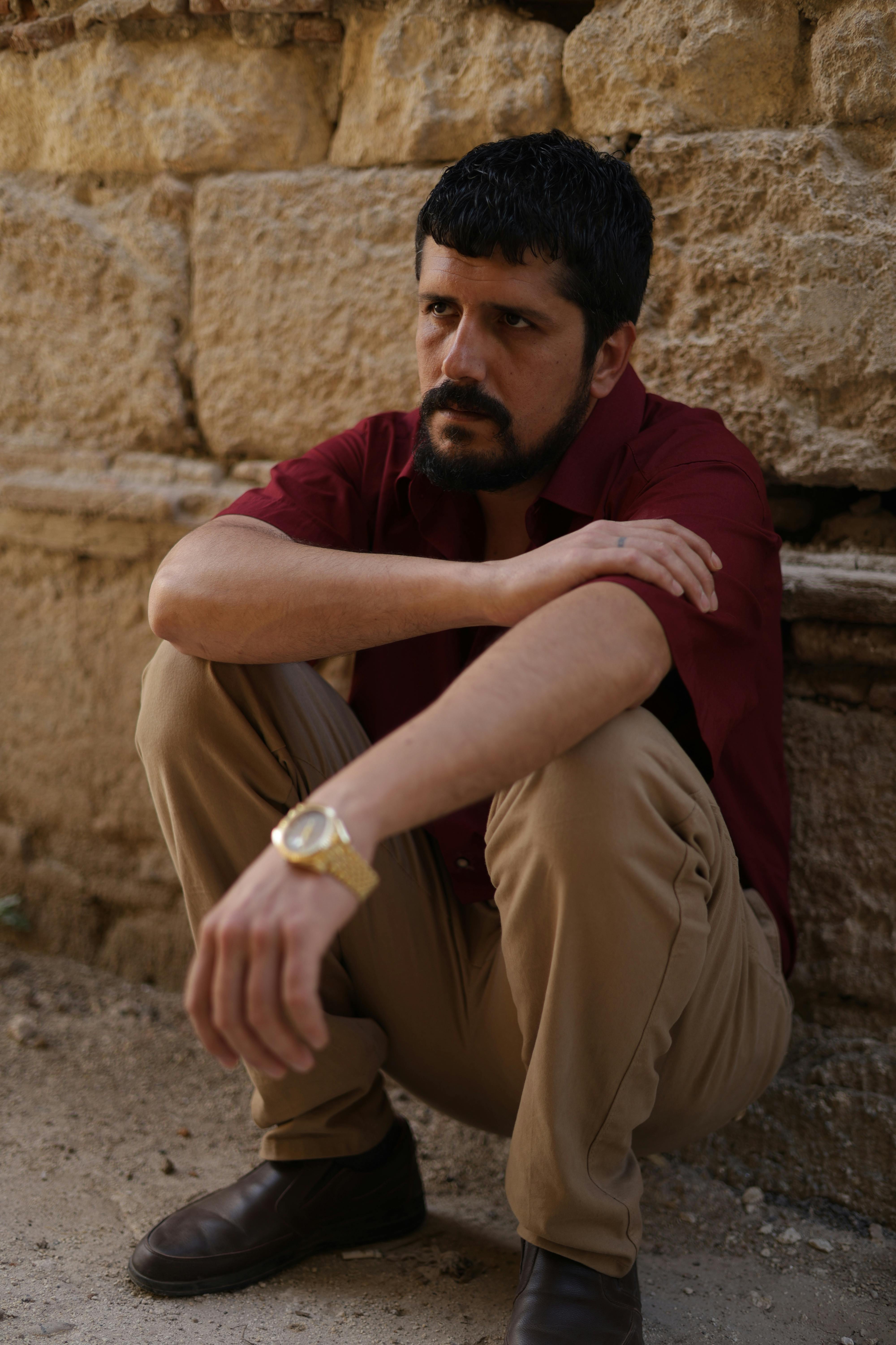 Thoughtful man in casual attire sitting against an ancient stone wall in Türkiye.