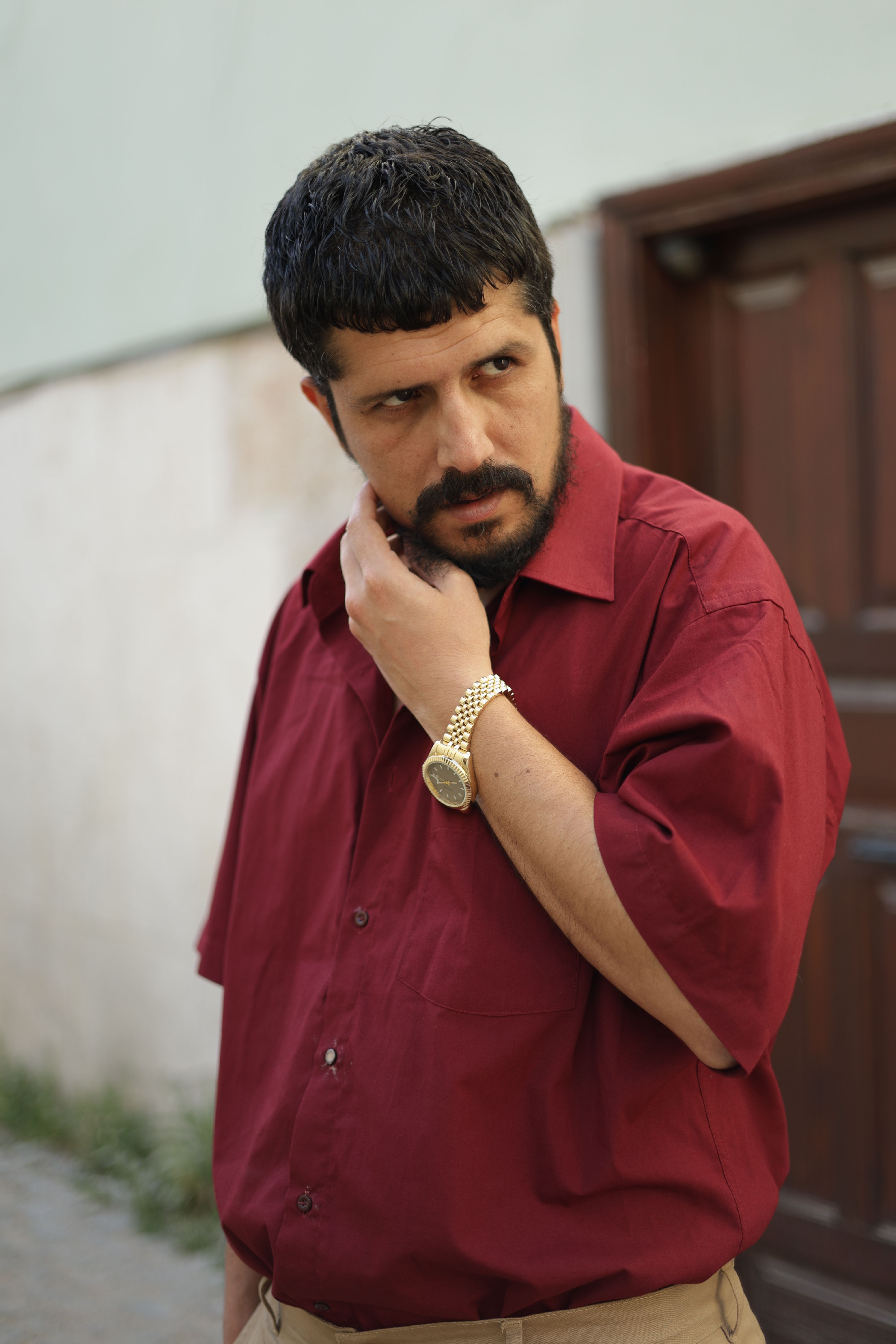 Portrait of a man in a red shirt standing outdoors in Türkiye, displaying thoughtful expression.