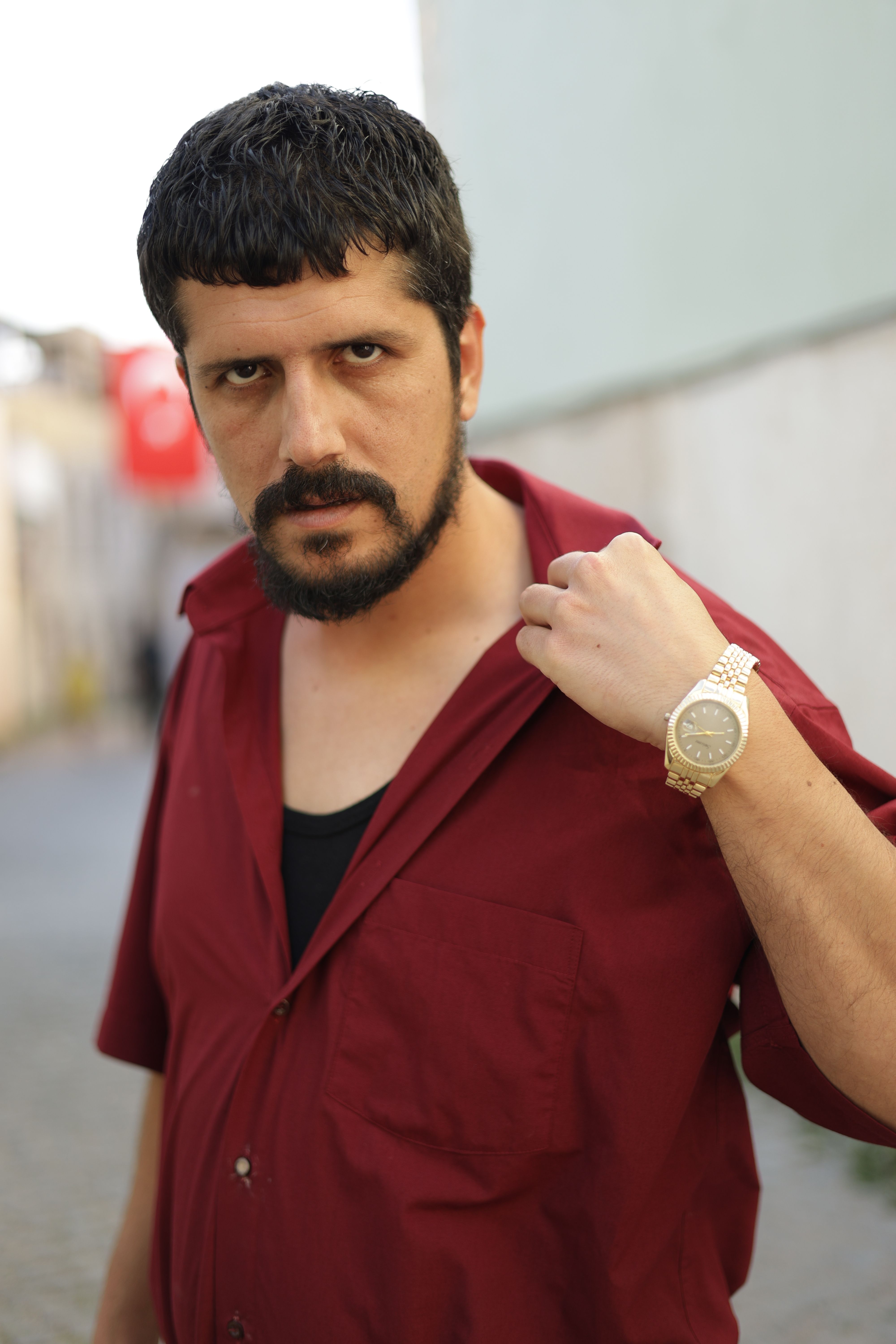 Portrait of a confident man posing outdoors in Türkiye, wearing a red shirt and watch.