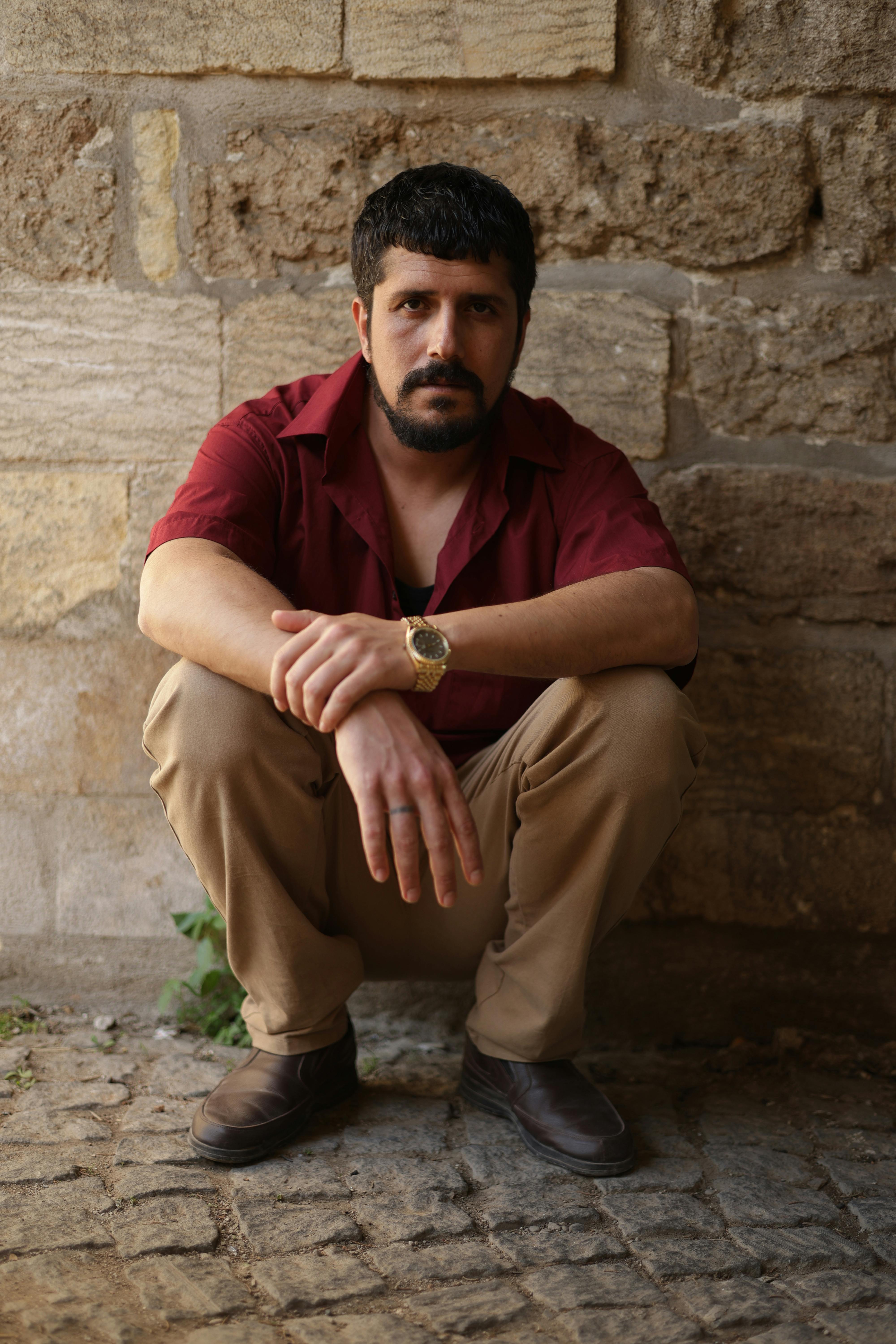 Portrait of a man in red shirt posing against a textured stone wall in Türkiye.