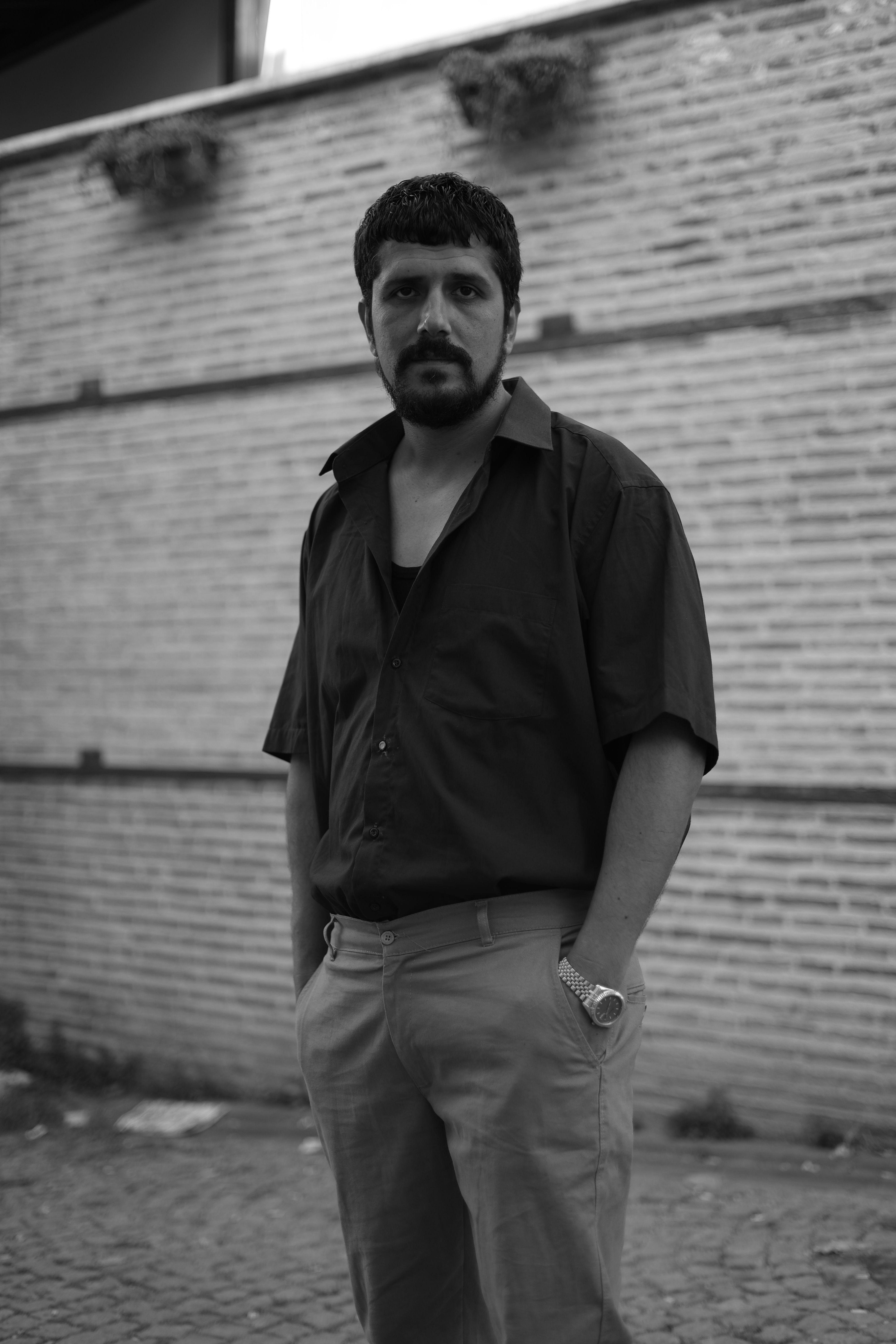 Candid black and white portrait of a man standing against a brick wall outdoors.