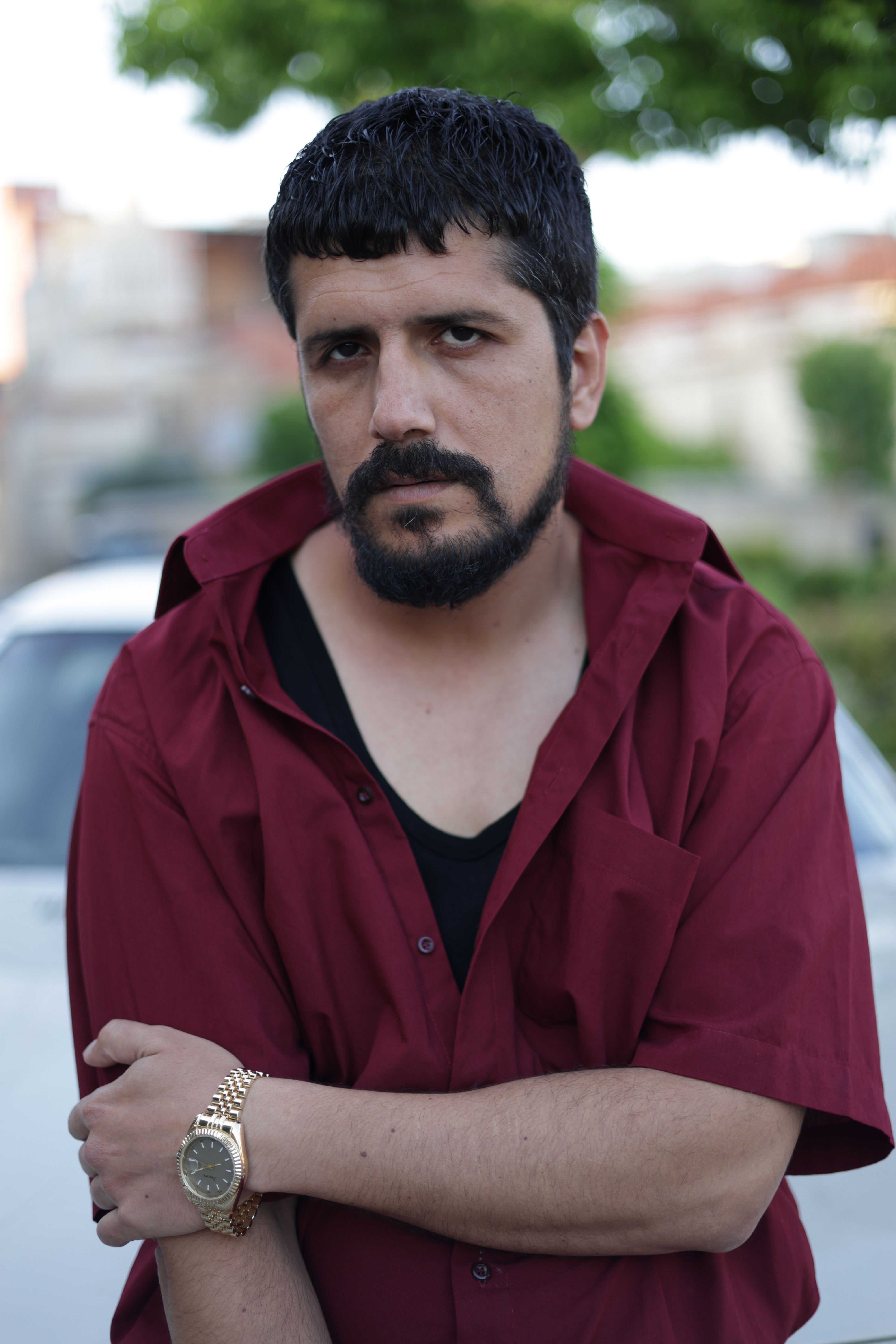 Casual portrait of a serious man outdoors in Türkiye wearing a red shirt and watch.