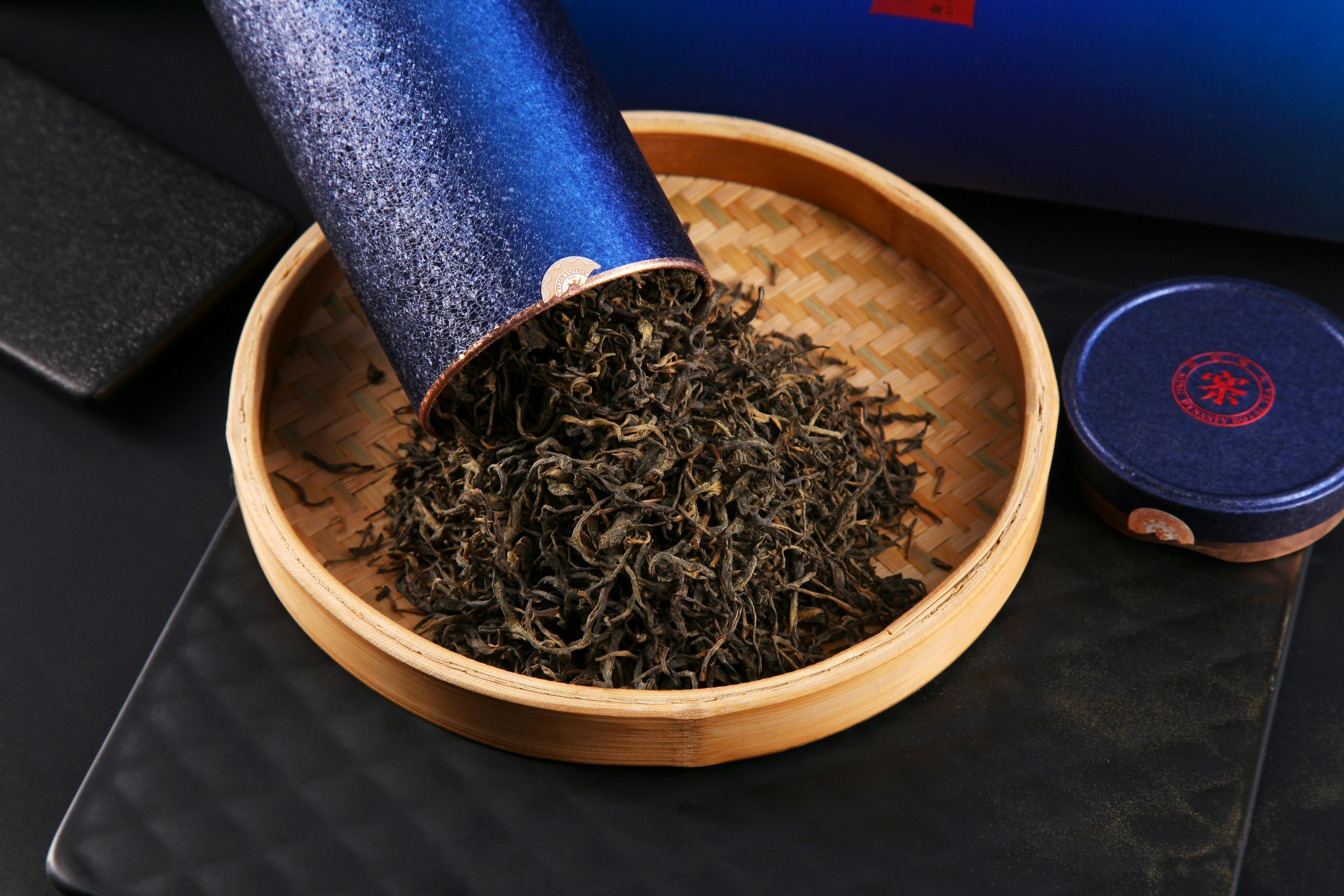 Elegant display of loose leaf tea spilling from a blue container into a bamboo plate.