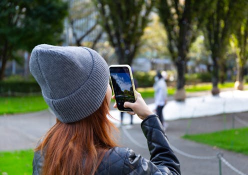 Young woman in Tokyo's Minato City capturing park scenery with her smartphone on a sunny day.